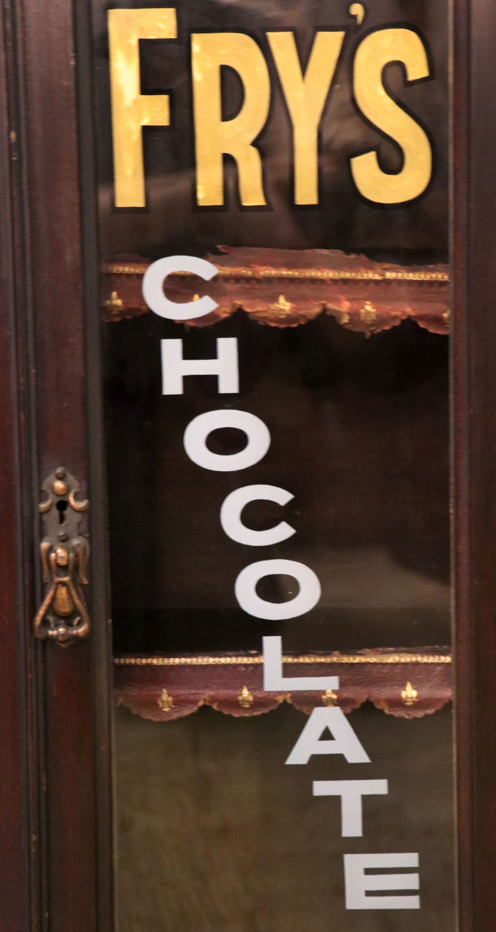 A dark mahogany Victorian display cabinet featuring glazed doors painted with Frys Cocoa and Chocolate advertising typography. View IV