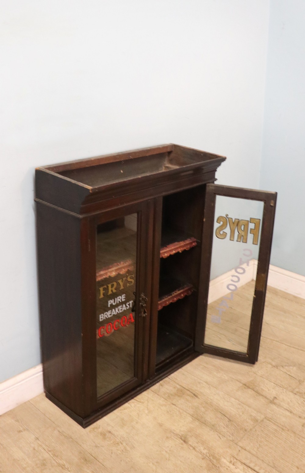 A dark mahogany Victorian display cabinet featuring glazed doors painted with Frys Cocoa and Chocolate advertising typography. View VI