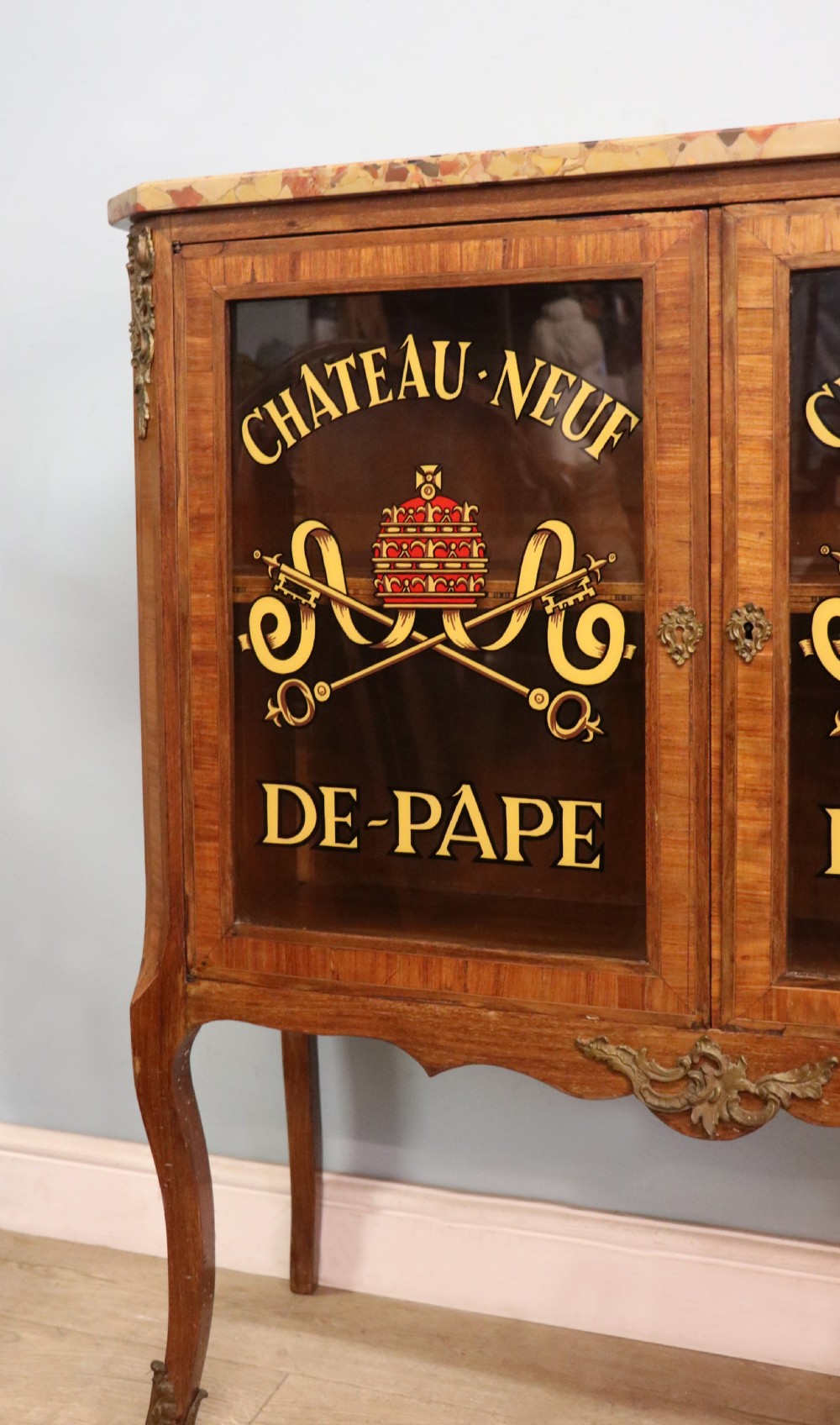 An early 20th-century French wooden display cabinet featuring a marble top, cabriole legs, gilt bronze mounts, and glass doors with hand-painted Chateauneuf-du-Pape lettering. View XVI