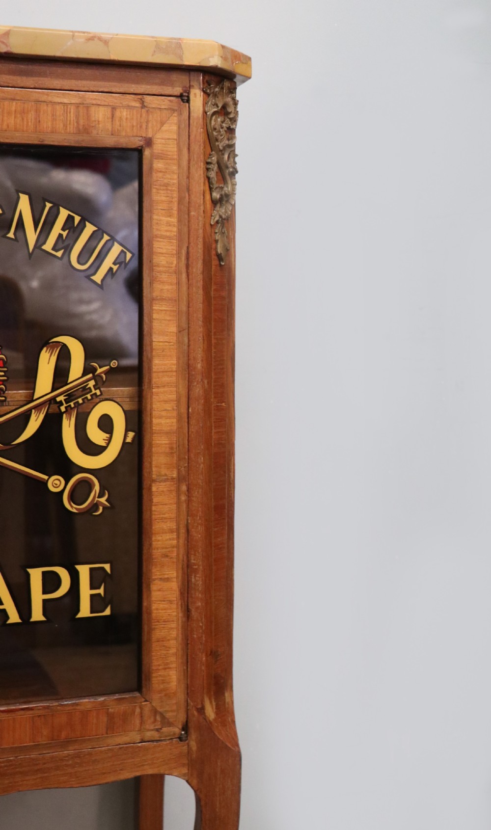 An early 20th-century French wooden display cabinet featuring a marble top, cabriole legs, gilt bronze mounts, and glass doors with hand-painted Chateauneuf-du-Pape lettering. View XVII
