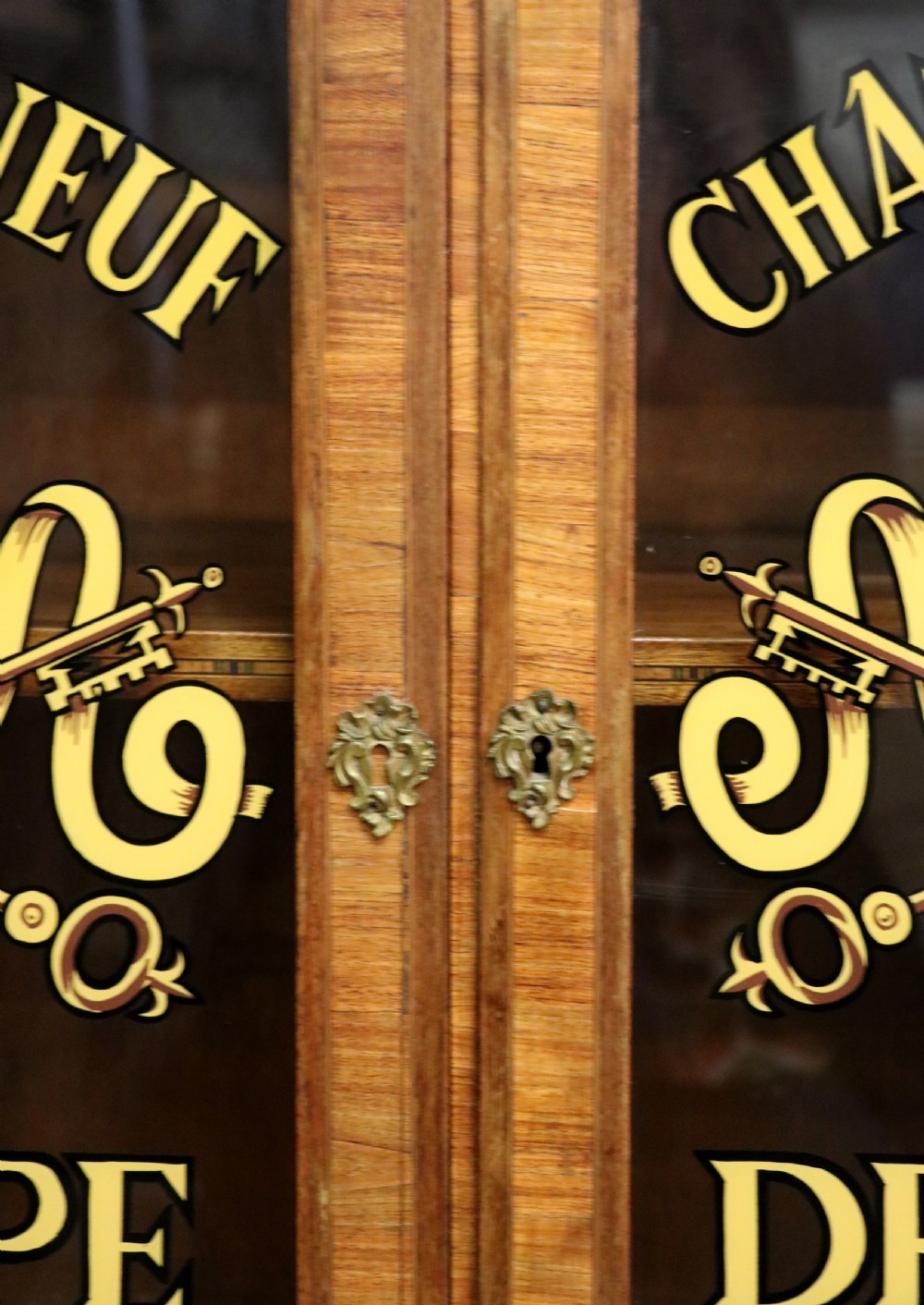 An early 20th-century French wooden display cabinet featuring a marble top, cabriole legs, gilt bronze mounts, and glass doors with hand-painted Chateauneuf-du-Pape lettering. View XVIII