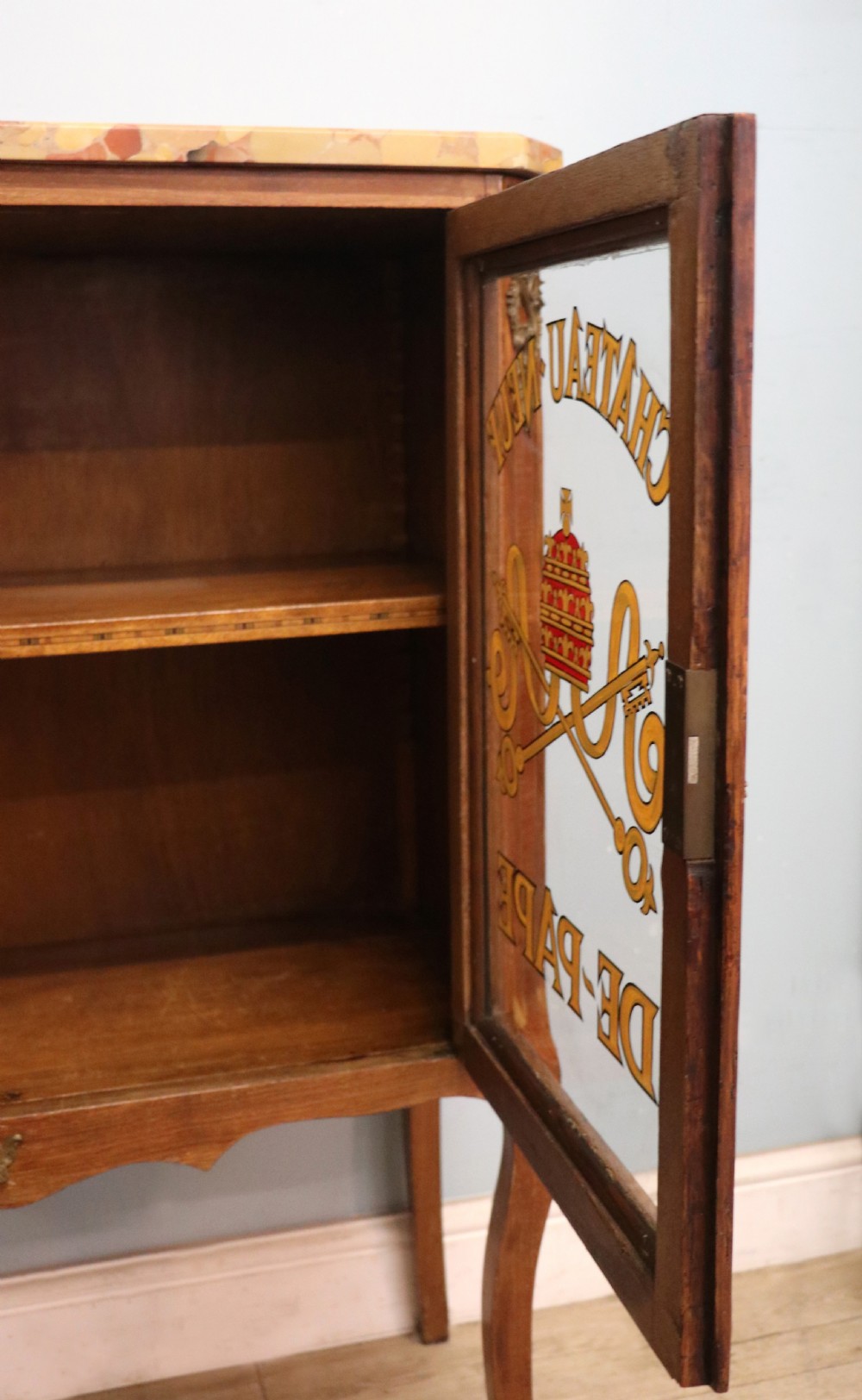 An early 20th-century French wooden display cabinet featuring a marble top, cabriole legs, gilt bronze mounts, and glass doors with hand-painted Chateauneuf-du-Pape lettering. View XXV