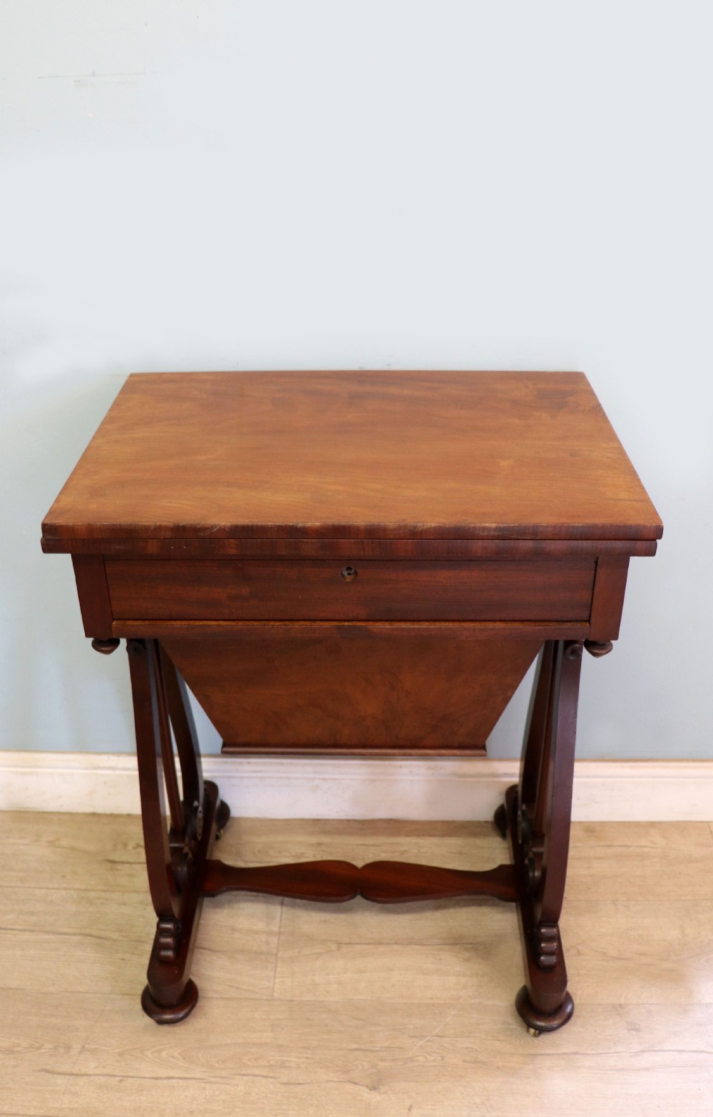 A nineteenth-century Victorian mahogany metamorphic sewing table featuring a hinged top, single drawer with brass escutcheon, tapered wooden storage bin, carved side supports, and brass castors. View II
