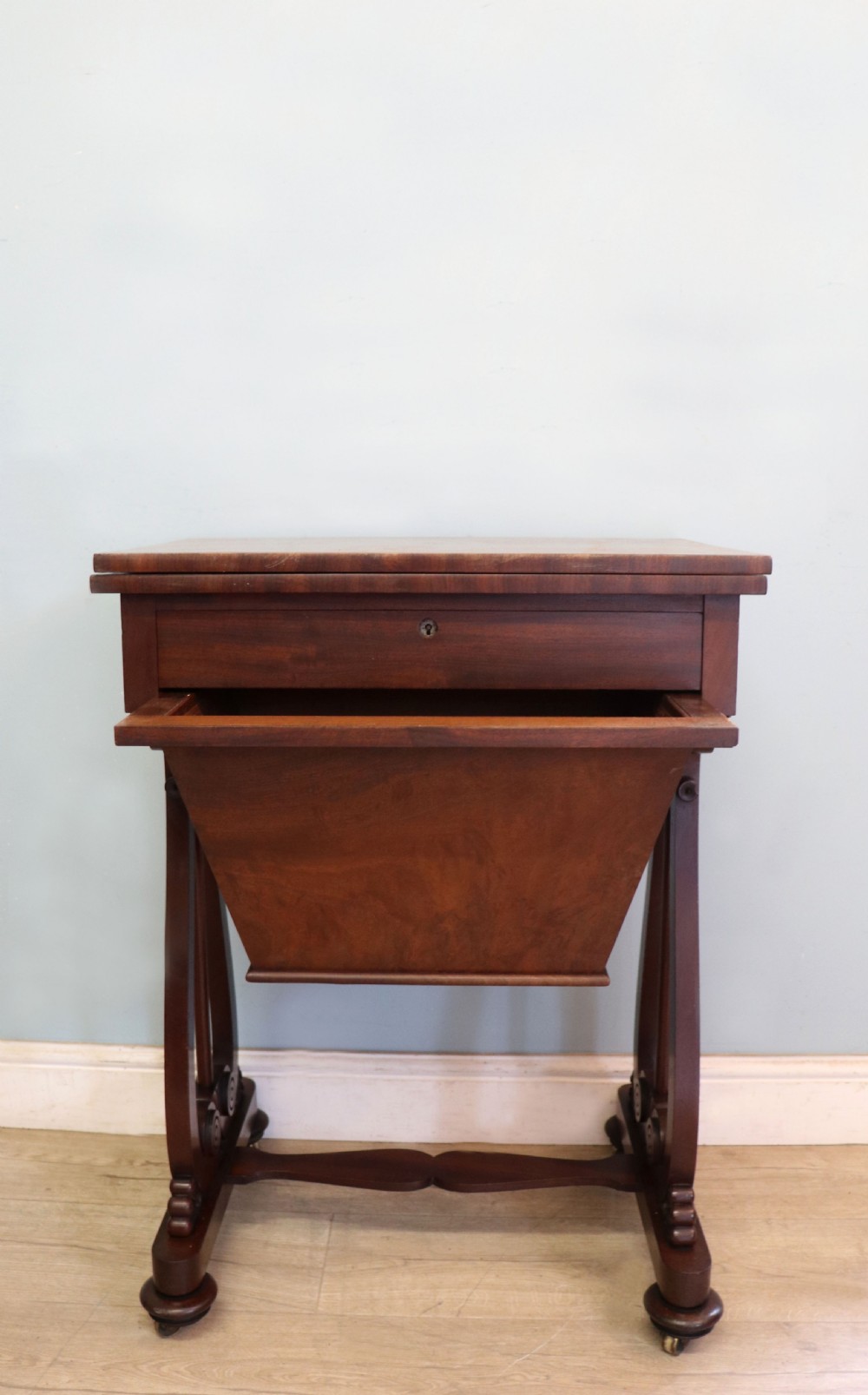 A nineteenth-century Victorian mahogany metamorphic sewing table featuring a hinged top, single drawer with brass escutcheon, tapered wooden storage bin, carved side supports, and brass castors. View III