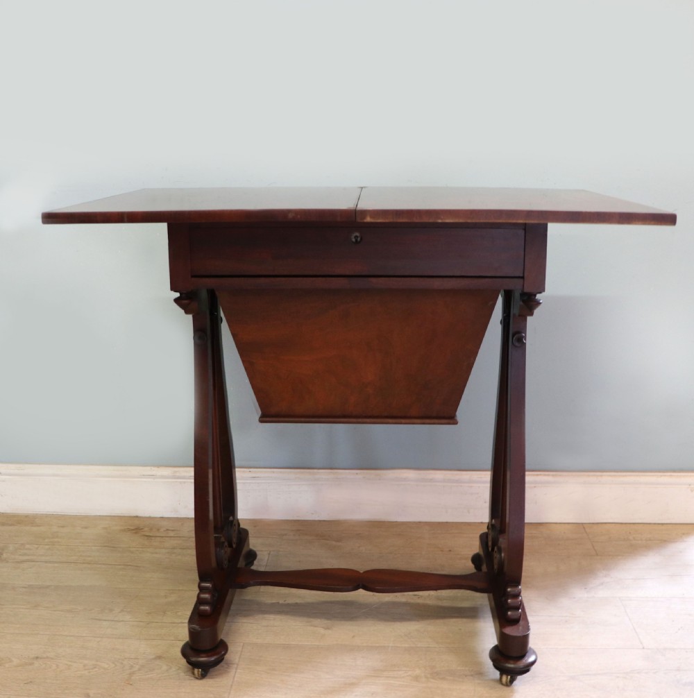 A nineteenth-century Victorian mahogany metamorphic sewing table featuring a hinged top, single drawer with brass escutcheon, tapered wooden storage bin, carved side supports, and brass castors. View VII