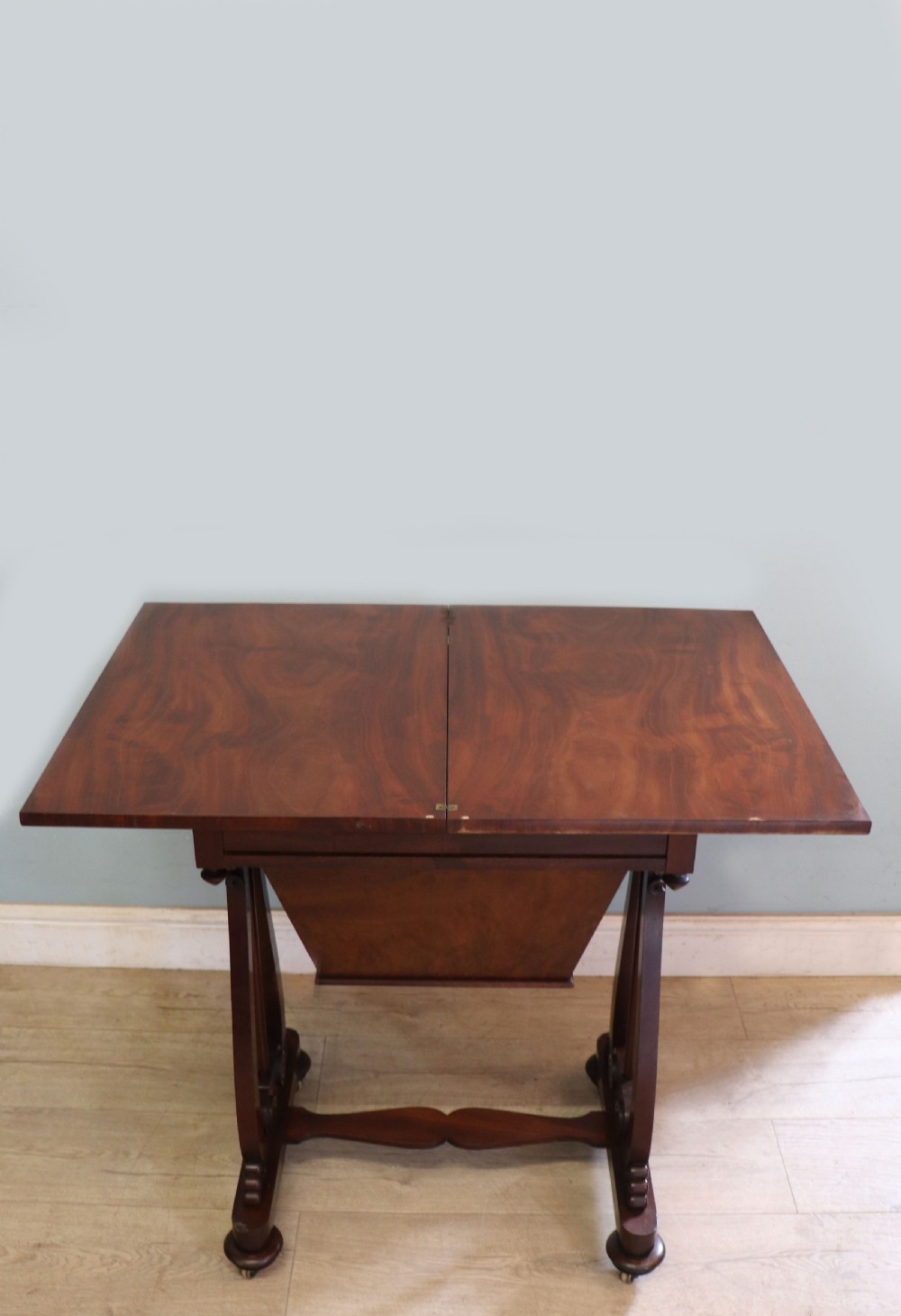 A nineteenth-century Victorian mahogany metamorphic sewing table featuring a hinged top, single drawer with brass escutcheon, tapered wooden storage bin, carved side supports, and brass castors. View VIII