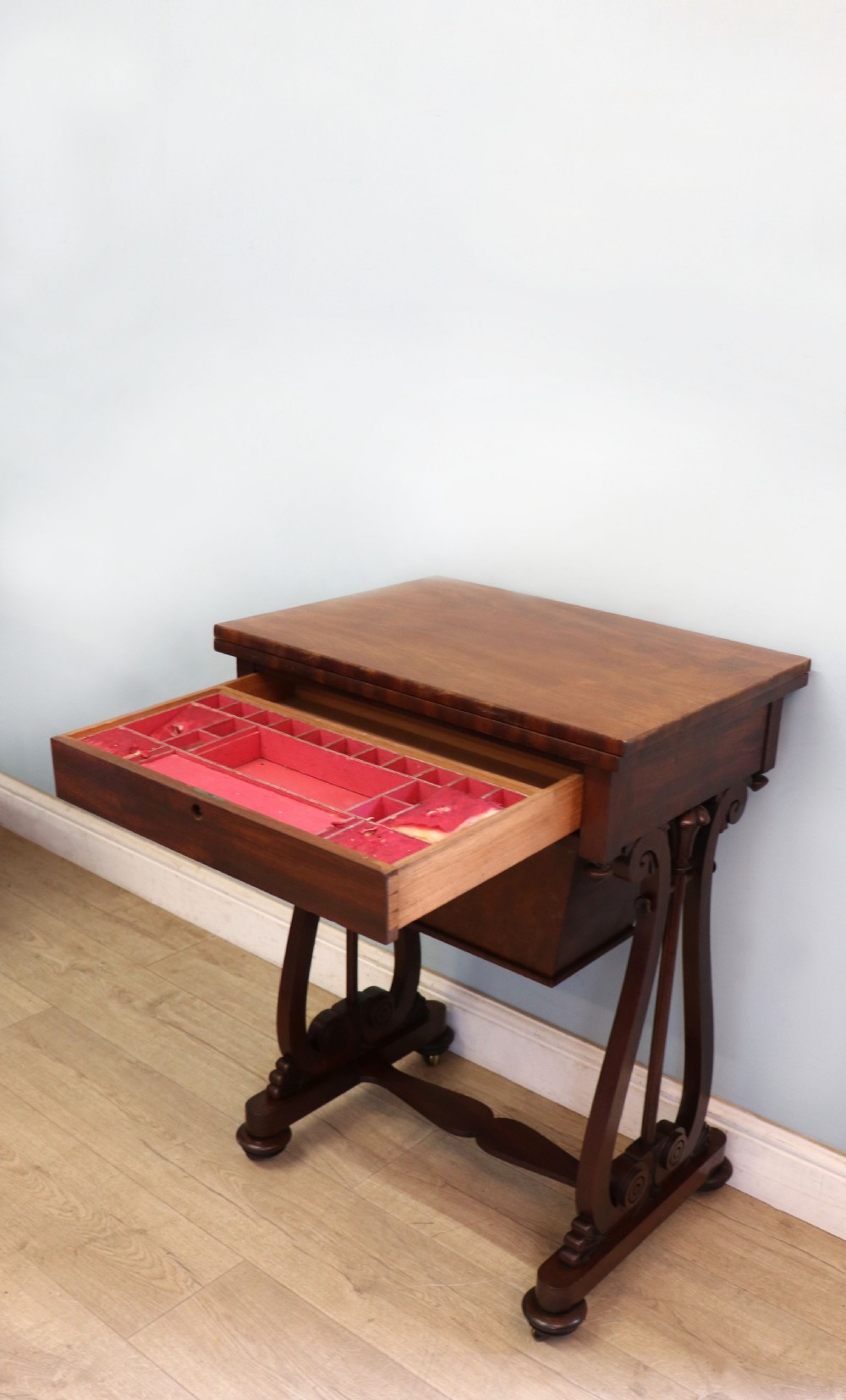 A nineteenth-century Victorian mahogany metamorphic sewing table featuring a hinged top, single drawer with brass escutcheon, tapered wooden storage bin, carved side supports, and brass castors. View XI