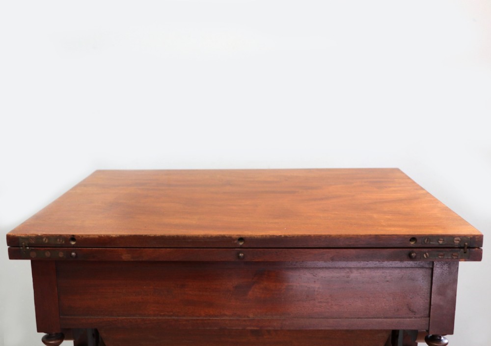 A nineteenth-century Victorian mahogany metamorphic sewing table featuring a hinged top, single drawer with brass escutcheon, tapered wooden storage bin, carved side supports, and brass castors. View XIV