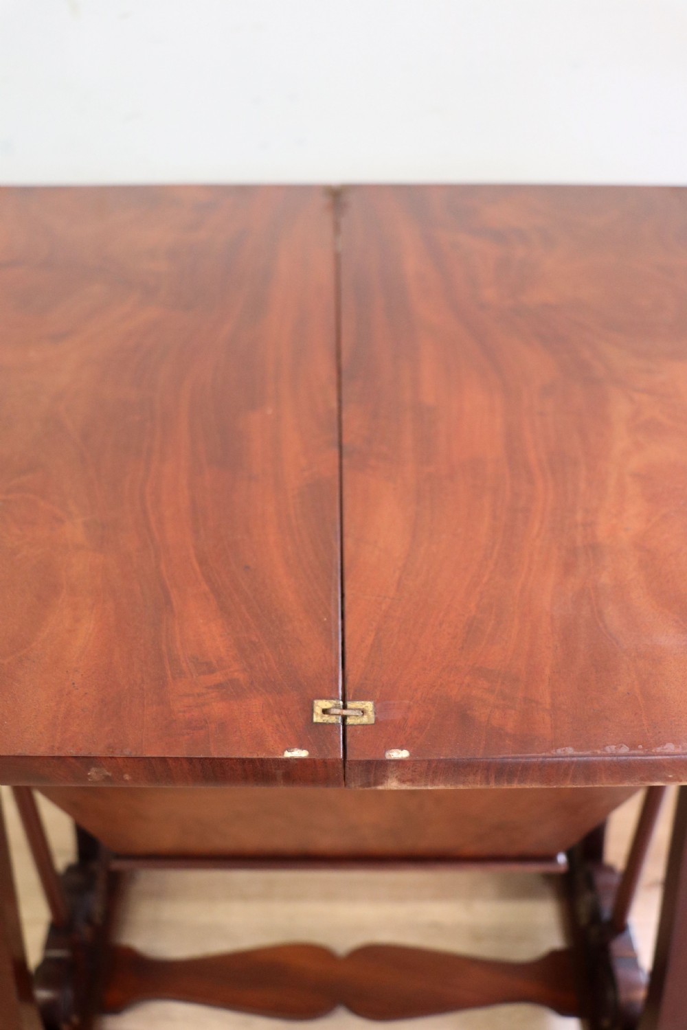 A nineteenth-century Victorian mahogany metamorphic sewing table featuring a hinged top, single drawer with brass escutcheon, tapered wooden storage bin, carved side supports, and brass castors. View XV