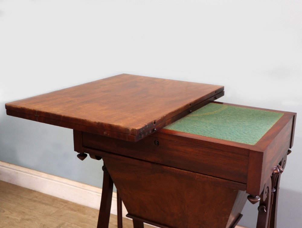 A nineteenth-century Victorian mahogany metamorphic sewing table featuring a hinged top, single drawer with brass escutcheon, tapered wooden storage bin, carved side supports, and brass castors. View XVIII
