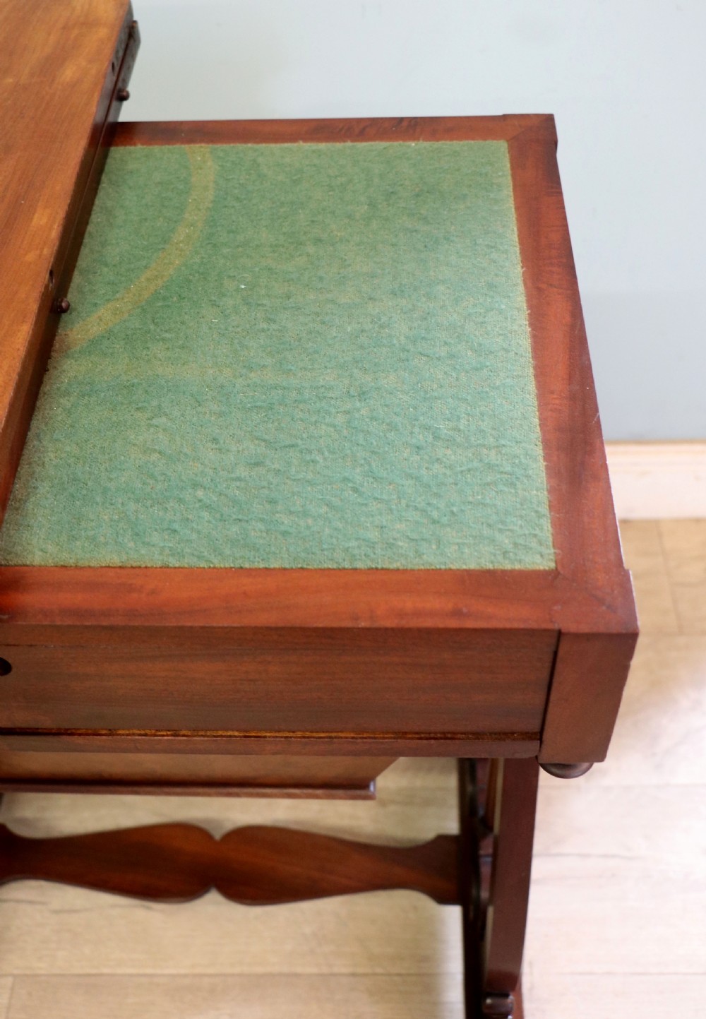 A nineteenth-century Victorian mahogany metamorphic sewing table featuring a hinged top, single drawer with brass escutcheon, tapered wooden storage bin, carved side supports, and brass castors. View XIX