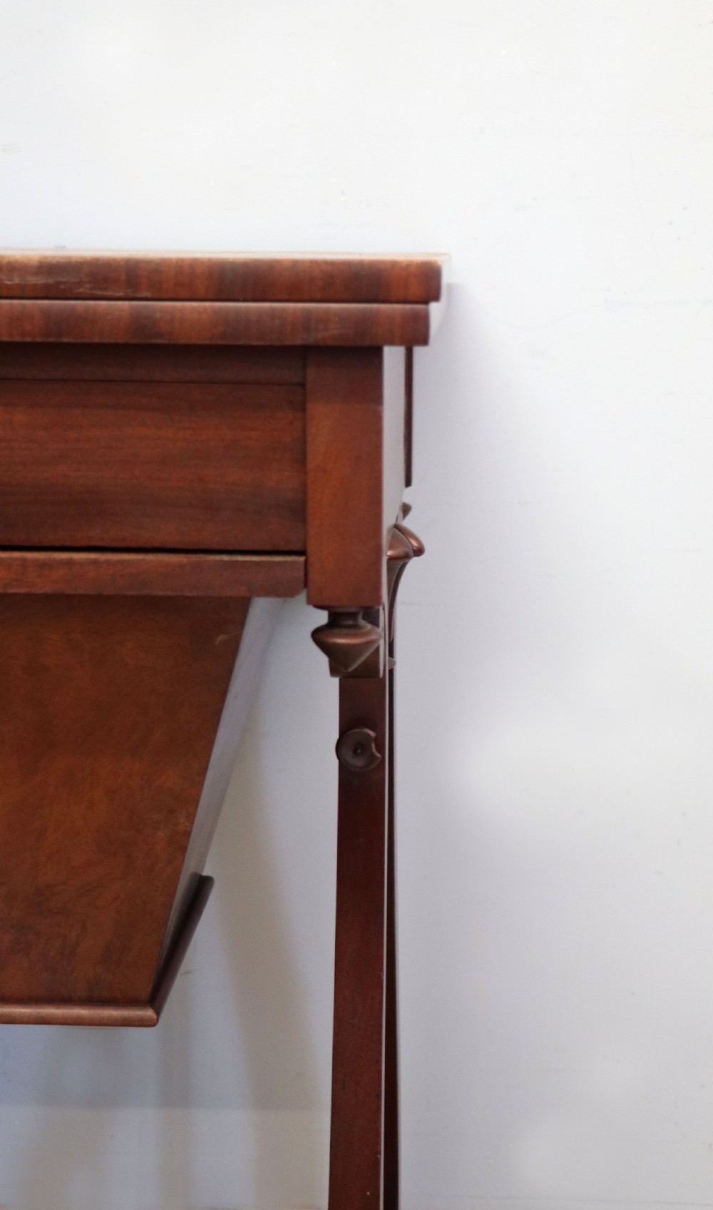 A nineteenth-century Victorian mahogany metamorphic sewing table featuring a hinged top, single drawer with brass escutcheon, tapered wooden storage bin, carved side supports, and brass castors. View XXI