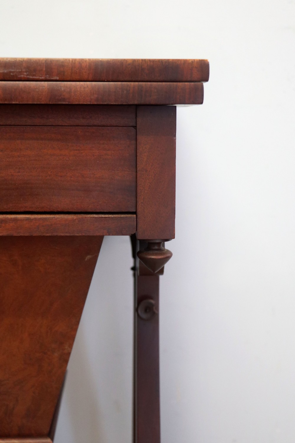 A nineteenth-century Victorian mahogany metamorphic sewing table featuring a hinged top, single drawer with brass escutcheon, tapered wooden storage bin, carved side supports, and brass castors. View XXII