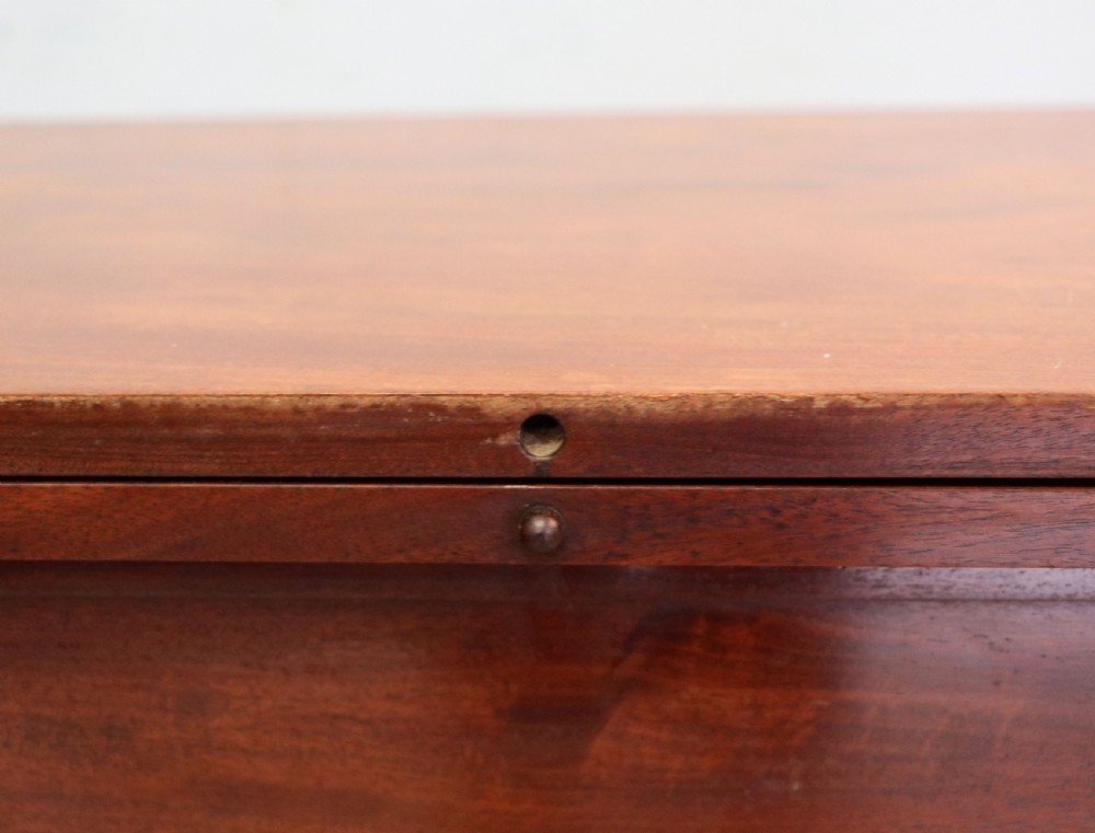 A nineteenth-century Victorian mahogany metamorphic sewing table featuring a hinged top, single drawer with brass escutcheon, tapered wooden storage bin, carved side supports, and brass castors. View XXIII