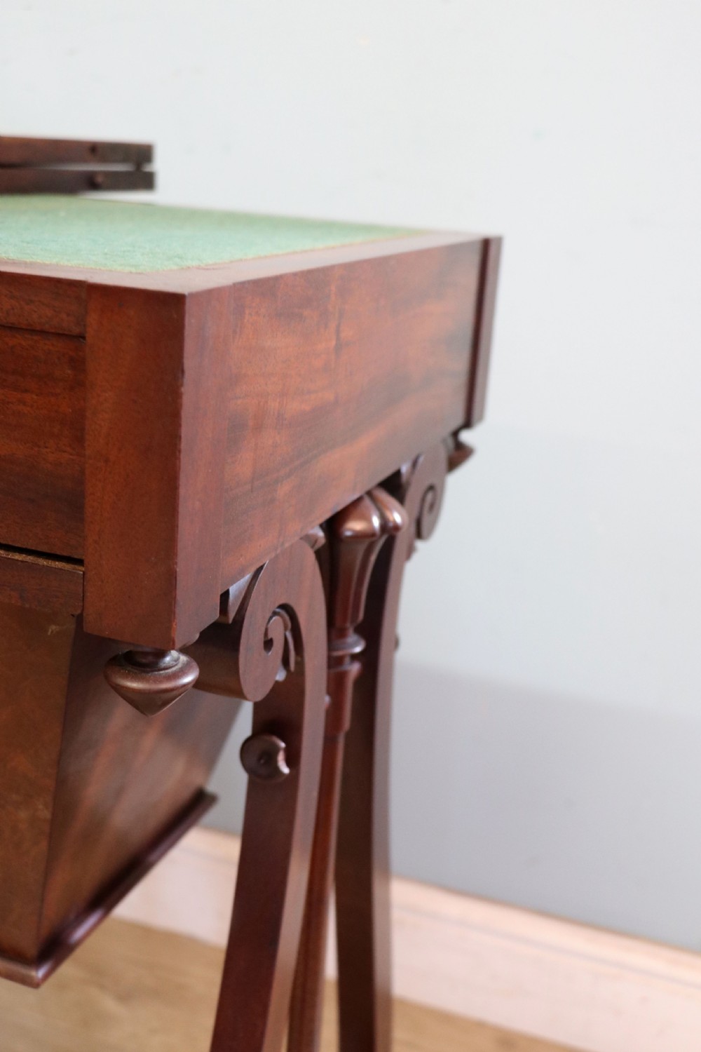 A nineteenth-century Victorian mahogany metamorphic sewing table featuring a hinged top, single drawer with brass escutcheon, tapered wooden storage bin, carved side supports, and brass castors. View XXVII