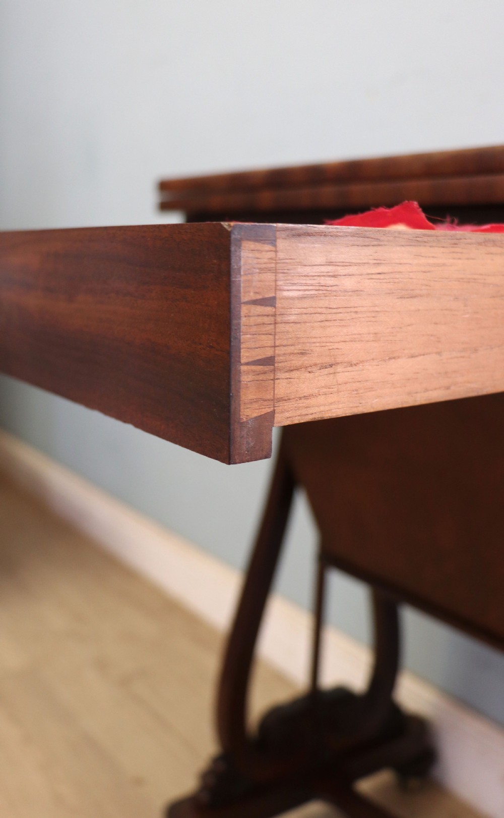 A nineteenth-century Victorian mahogany metamorphic sewing table featuring a hinged top, single drawer with brass escutcheon, tapered wooden storage bin, carved side supports, and brass castors. View XXVIII