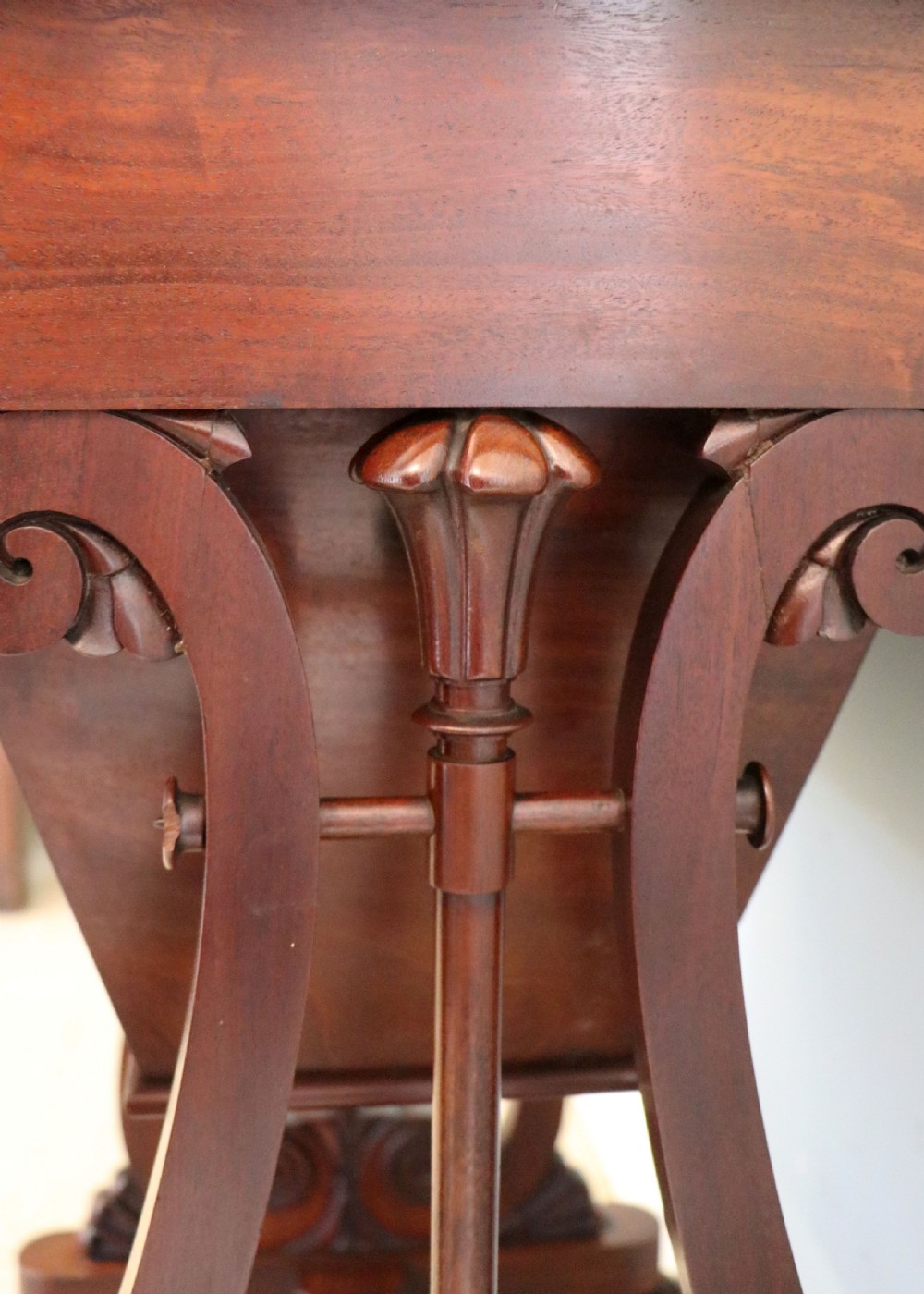 A nineteenth-century Victorian mahogany metamorphic sewing table featuring a hinged top, single drawer with brass escutcheon, tapered wooden storage bin, carved side supports, and brass castors. View XXIX