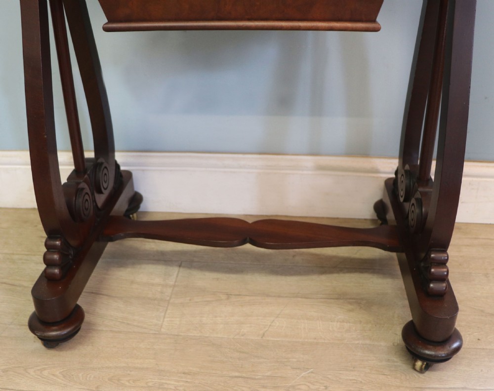 A nineteenth-century Victorian mahogany metamorphic sewing table featuring a hinged top, single drawer with brass escutcheon, tapered wooden storage bin, carved side supports, and brass castors. View XXX