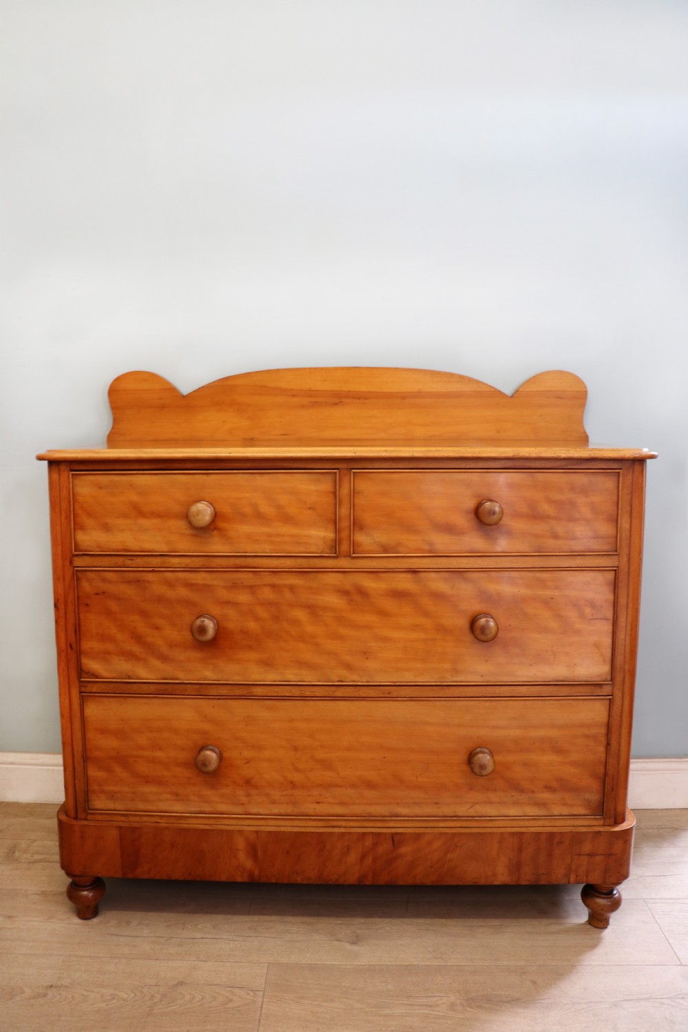 A Victorian satin birch chest of drawers featuring a shaped gallery backboard, two short over two long drawers with turned knobs, resting on a plinth base.