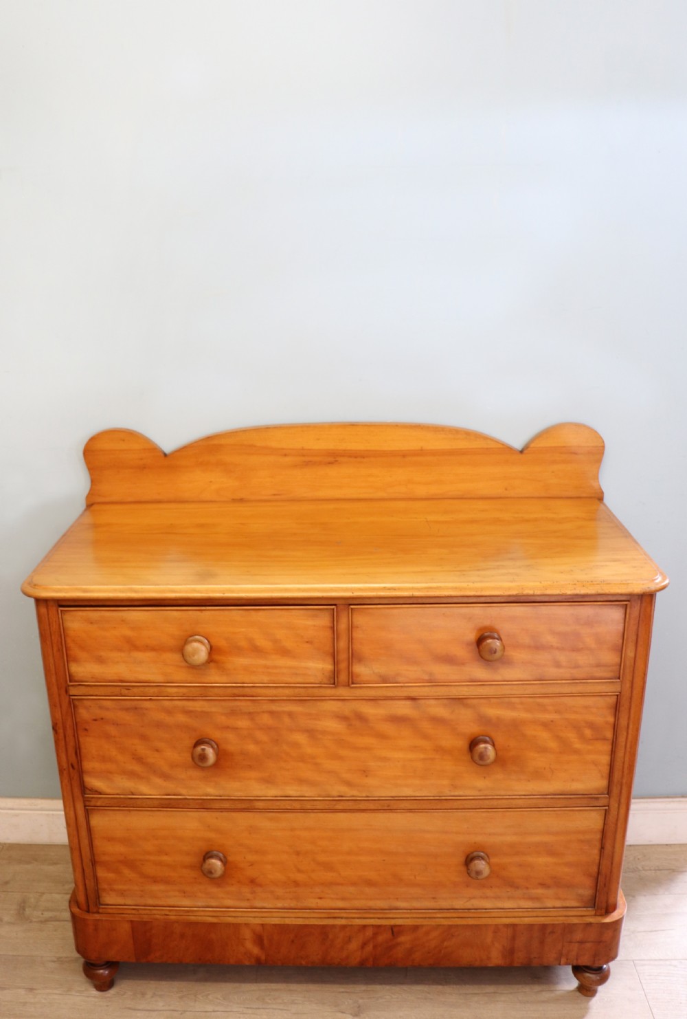 A Victorian satin birch chest of drawers featuring a shaped gallery backboard, two short over two long drawers with turned knobs, resting on a plinth base. View II