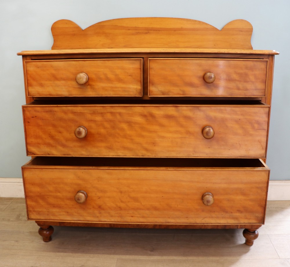 A Victorian satin birch chest of drawers featuring a shaped gallery backboard, two short over two long drawers with turned knobs, resting on a plinth base. View III