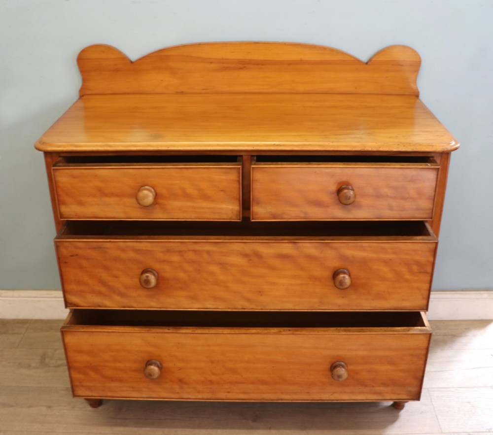 A Victorian satin birch chest of drawers featuring a shaped gallery backboard, two short over two long drawers with turned knobs, resting on a plinth base. View V