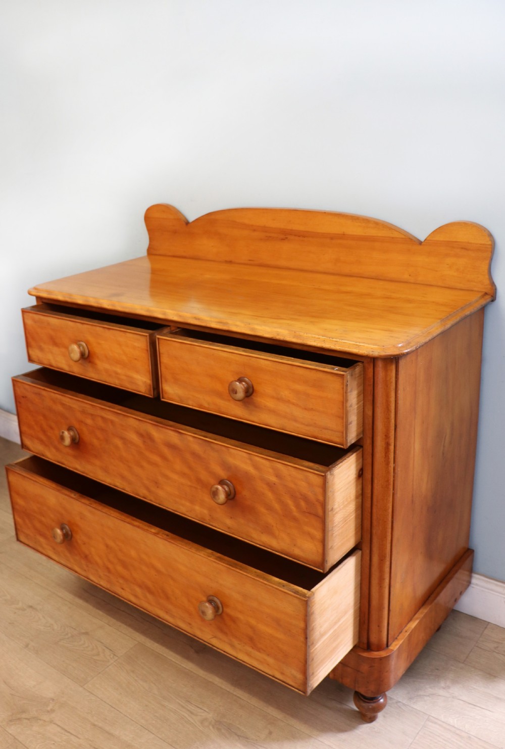 A Victorian satin birch chest of drawers featuring a shaped gallery backboard, two short over two long drawers with turned knobs, resting on a plinth base. View VI