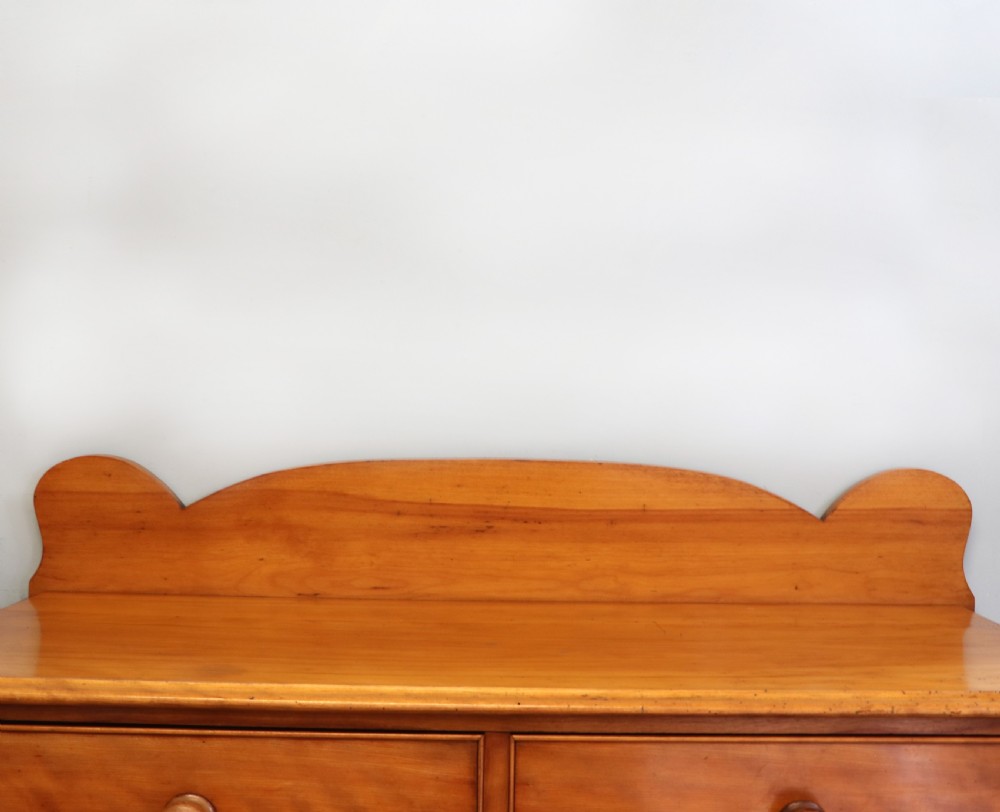 A Victorian satin birch chest of drawers featuring a shaped gallery backboard, two short over two long drawers with turned knobs, resting on a plinth base. View VII