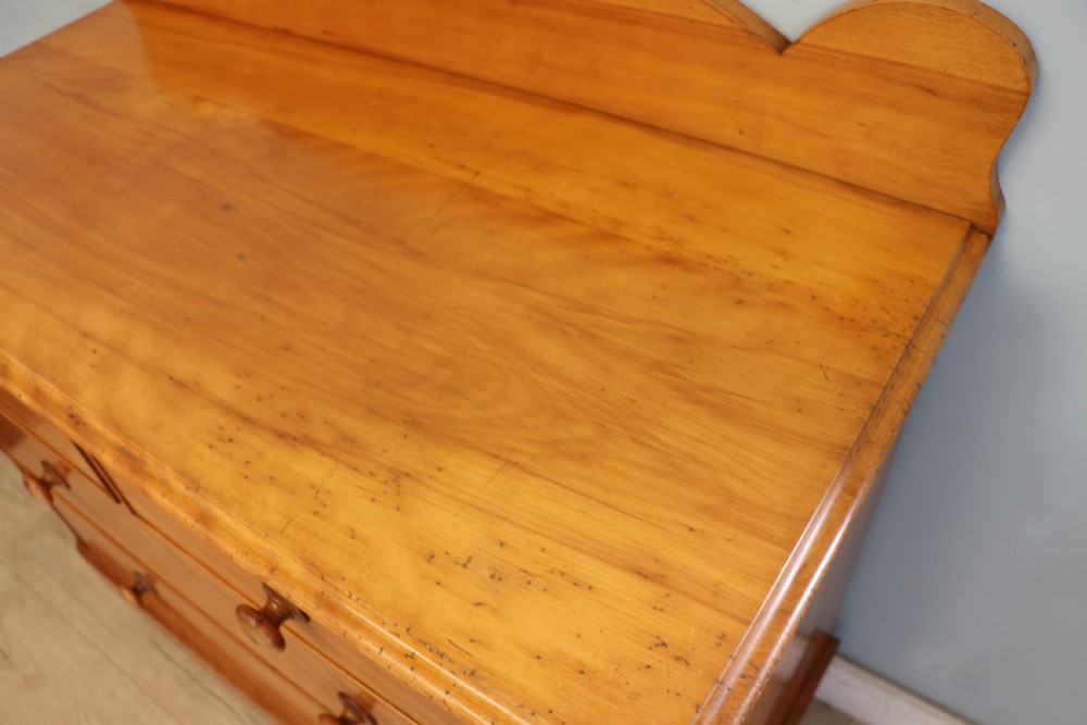 A Victorian satin birch chest of drawers featuring a shaped gallery backboard, two short over two long drawers with turned knobs, resting on a plinth base. View IX