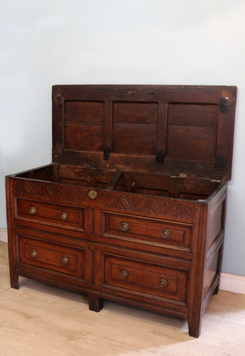 An 18th-century dark oak coffer with a hinged top lid, a carved upper frieze, and panelled lower drawers featuring brass drop handles. View II