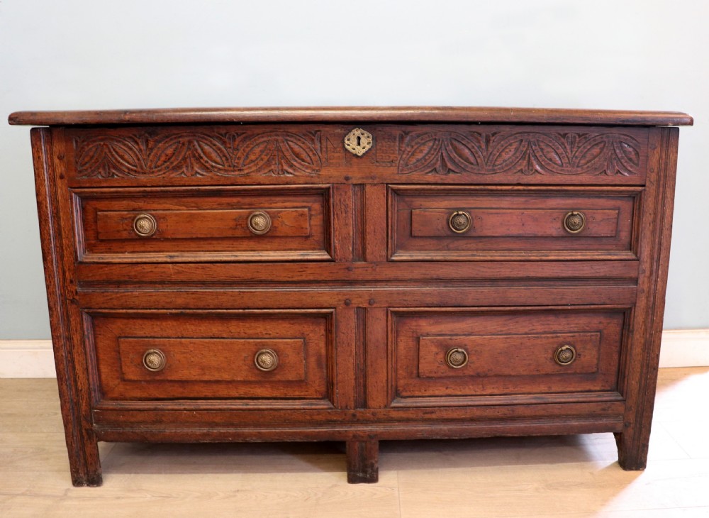 An 18th-century dark oak coffer with a hinged top lid, a carved upper frieze, and panelled lower drawers featuring brass drop handles. View III
