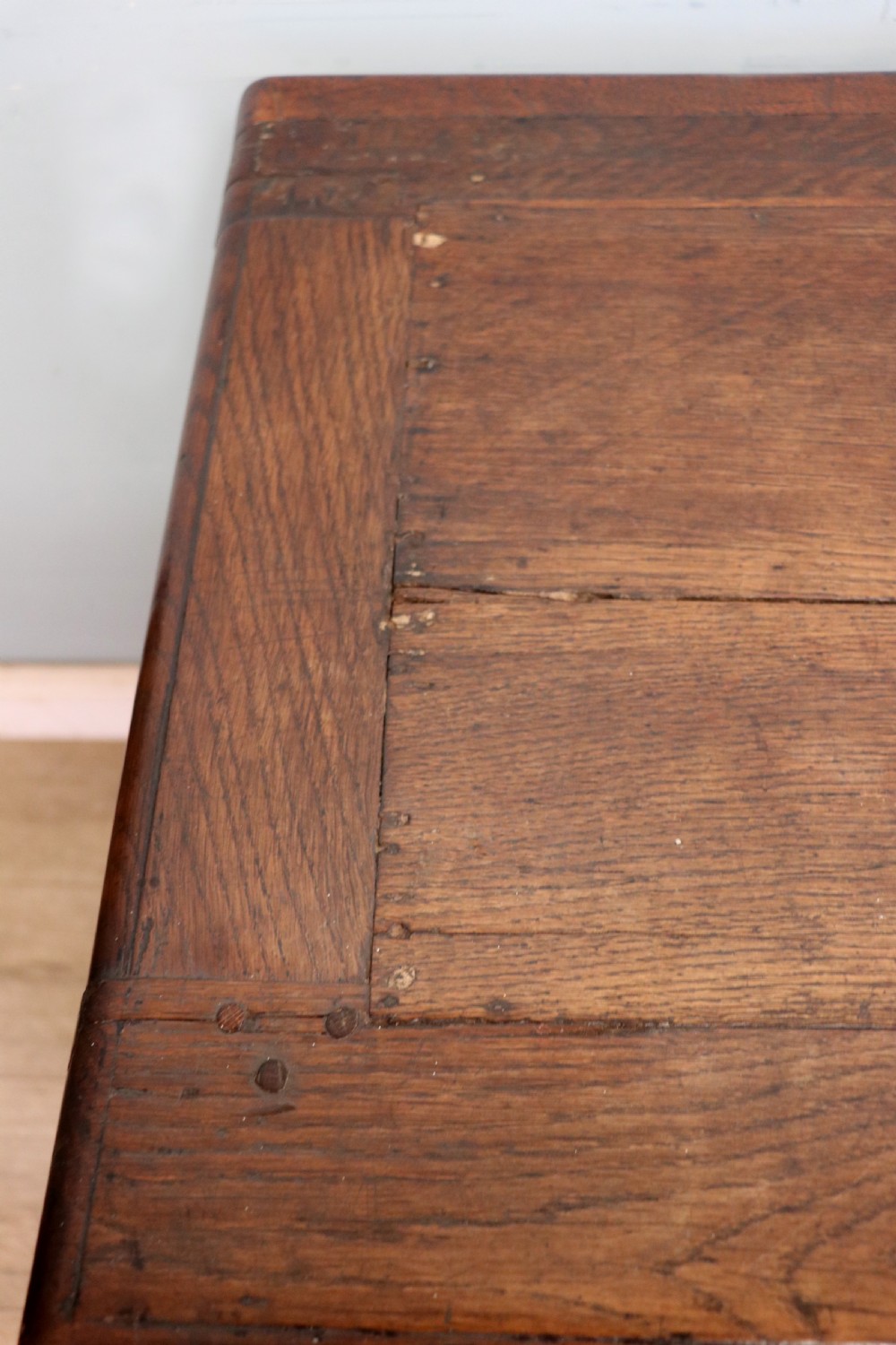 An 18th-century dark oak coffer with a hinged top lid, a carved upper frieze, and panelled lower drawers featuring brass drop handles. View VI