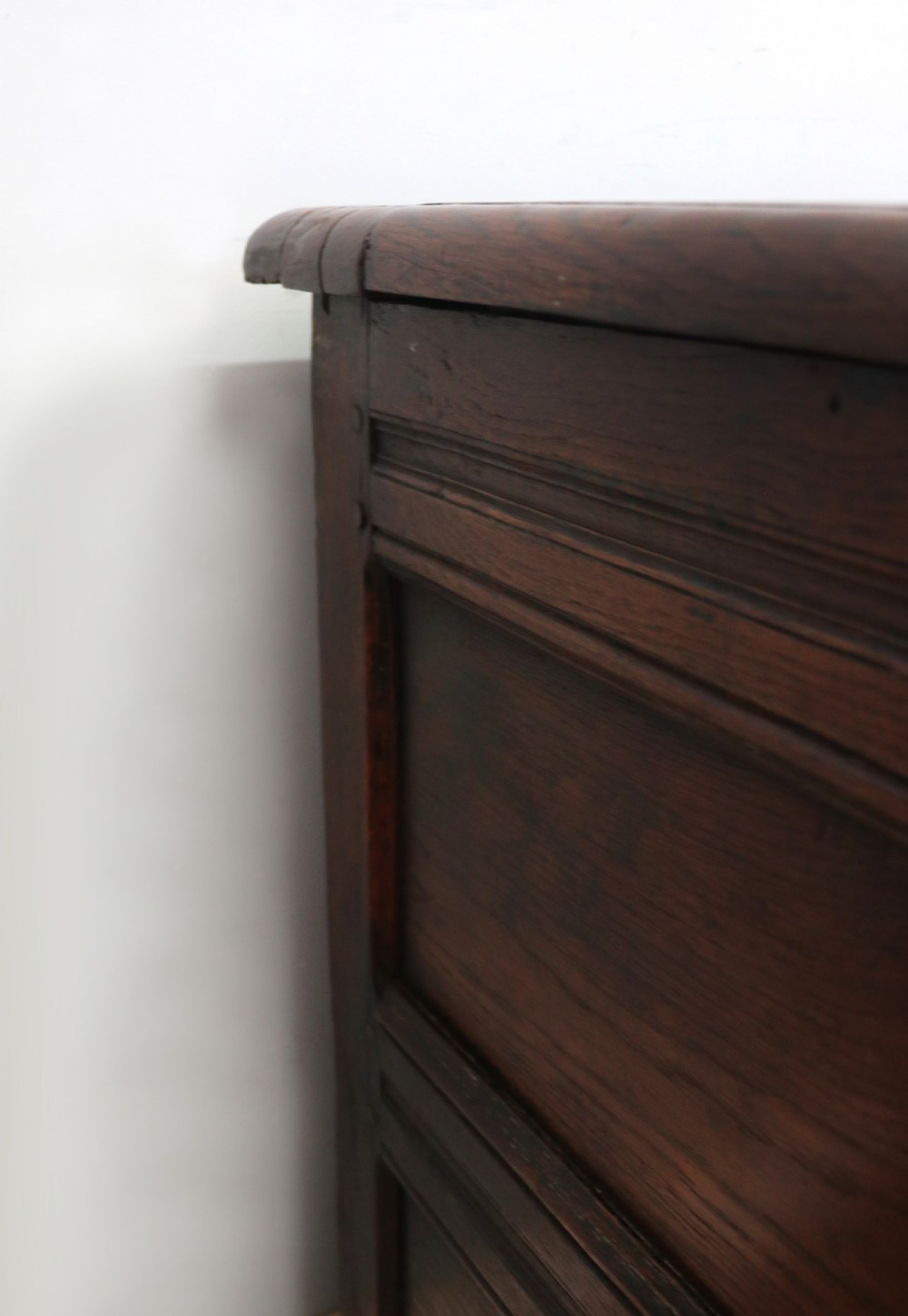 An 18th-century dark oak coffer with a hinged top lid, a carved upper frieze, and panelled lower drawers featuring brass drop handles. View VII