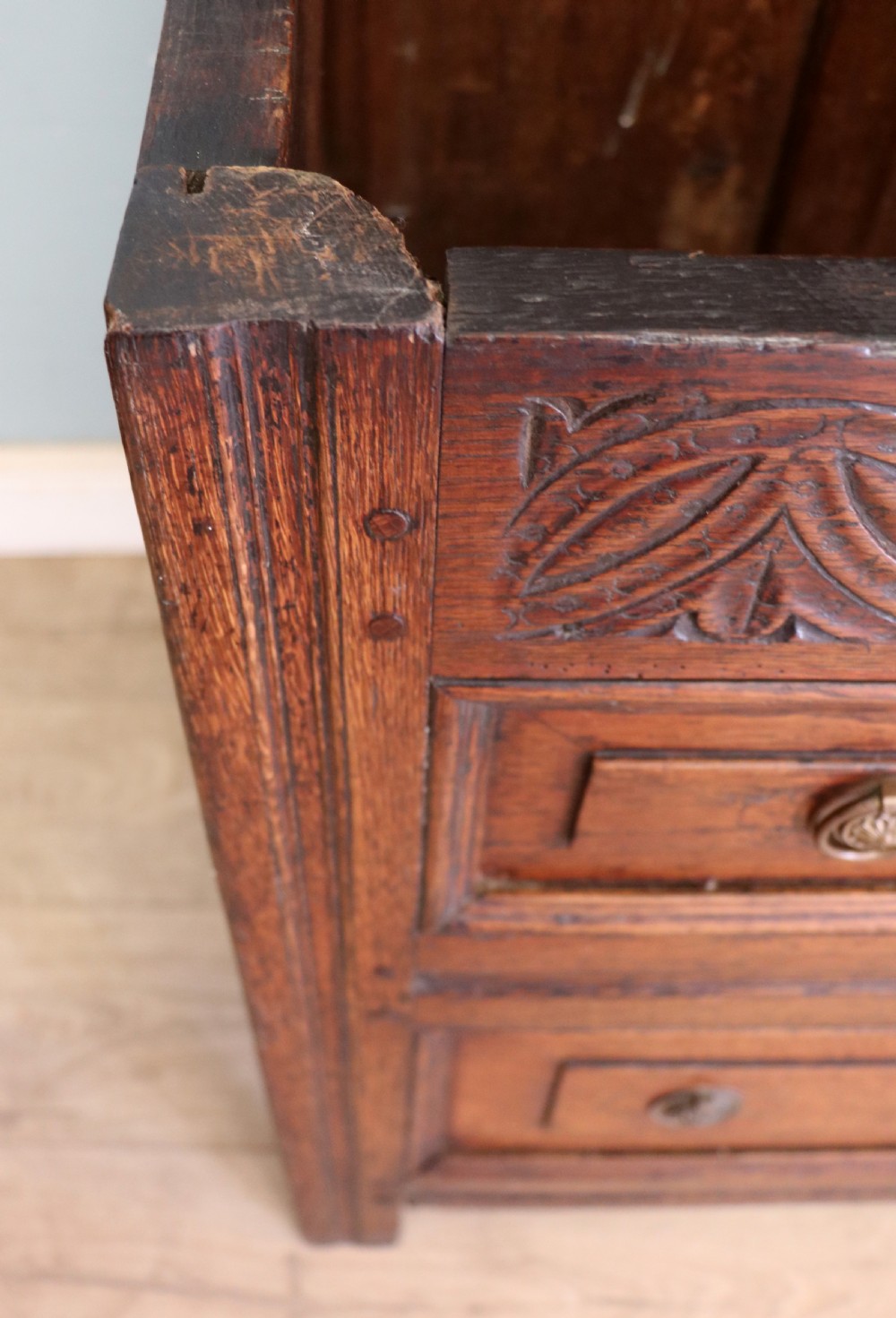 An 18th-century dark oak coffer with a hinged top lid, a carved upper frieze, and panelled lower drawers featuring brass drop handles. View XII