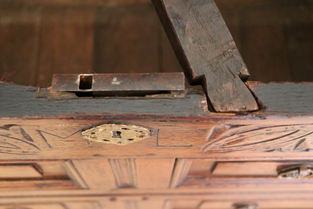An 18th-century dark oak coffer with a hinged top lid, a carved upper frieze, and panelled lower drawers featuring brass drop handles. View XXI