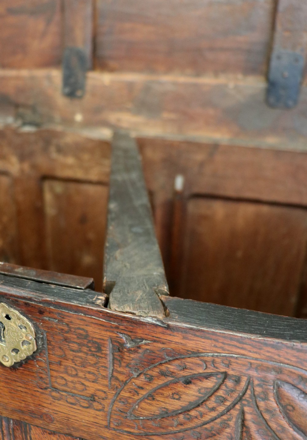 An 18th-century dark oak coffer with a hinged top lid, a carved upper frieze, and panelled lower drawers featuring brass drop handles. View XXIII