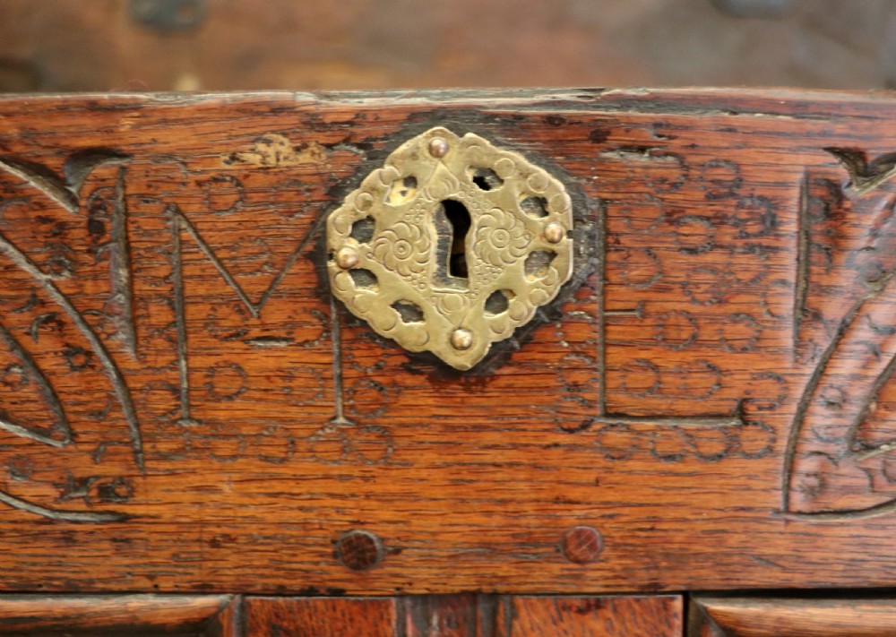 An 18th-century dark oak coffer with a hinged top lid, a carved upper frieze, and panelled lower drawers featuring brass drop handles. View XXVI