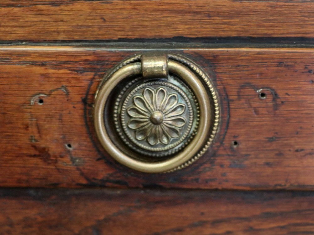 An 18th-century dark oak coffer with a hinged top lid, a carved upper frieze, and panelled lower drawers featuring brass drop handles. View XXVIII