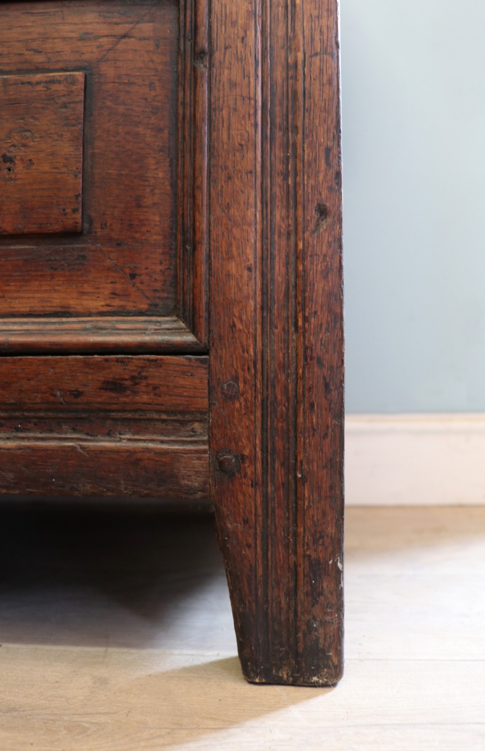 An 18th-century dark oak coffer with a hinged top lid, a carved upper frieze, and panelled lower drawers featuring brass drop handles. View XXX