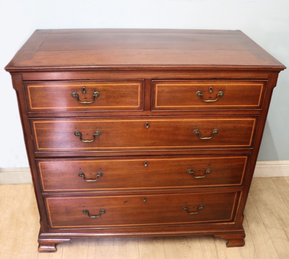 A Georgian Revival mahogany chest of drawers featuring two short drawers over three long drawers with decorative inlay and brass handles.
