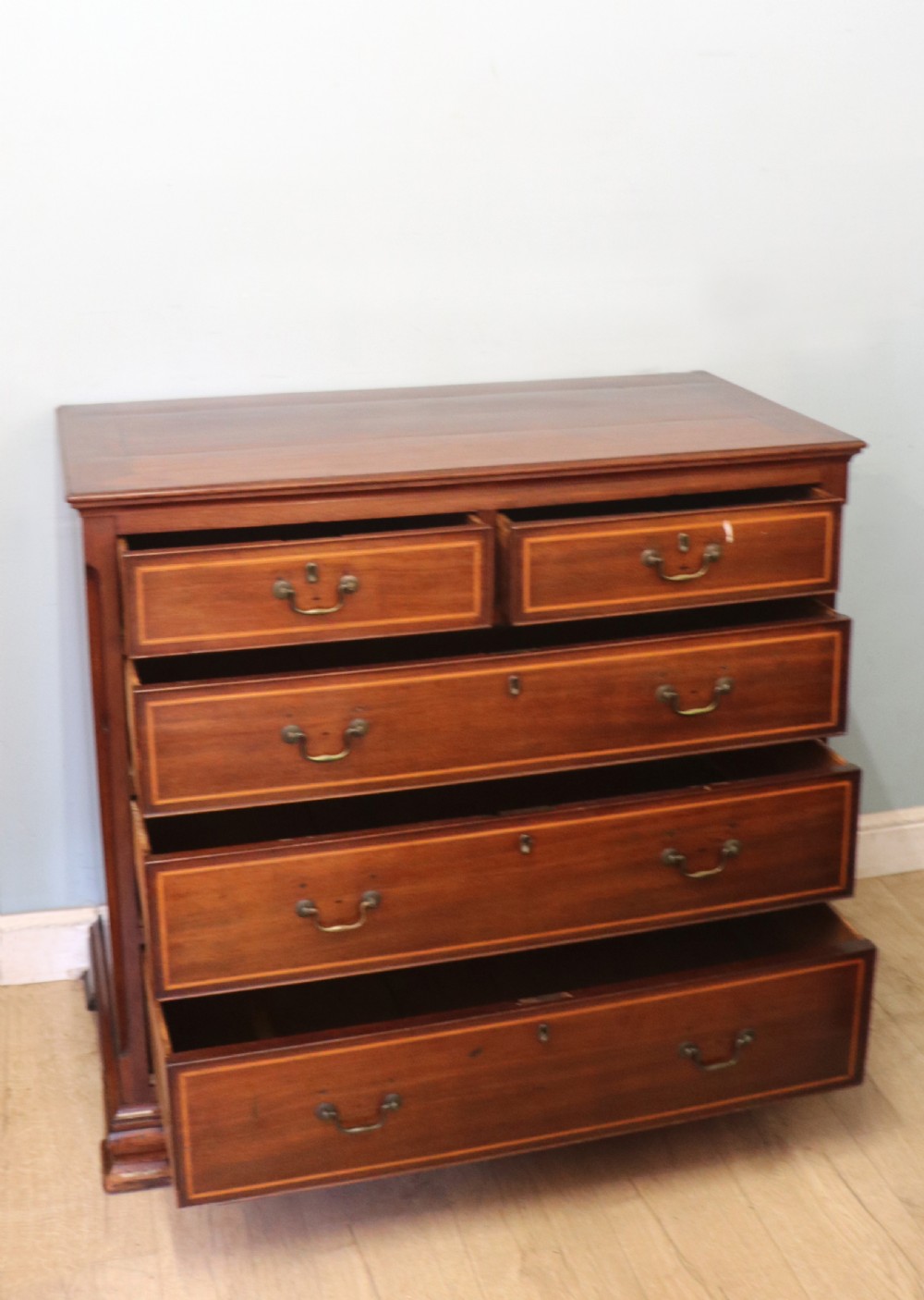 A Georgian Revival mahogany chest of drawers featuring two short drawers over three long drawers with decorative inlay and brass handles. View V