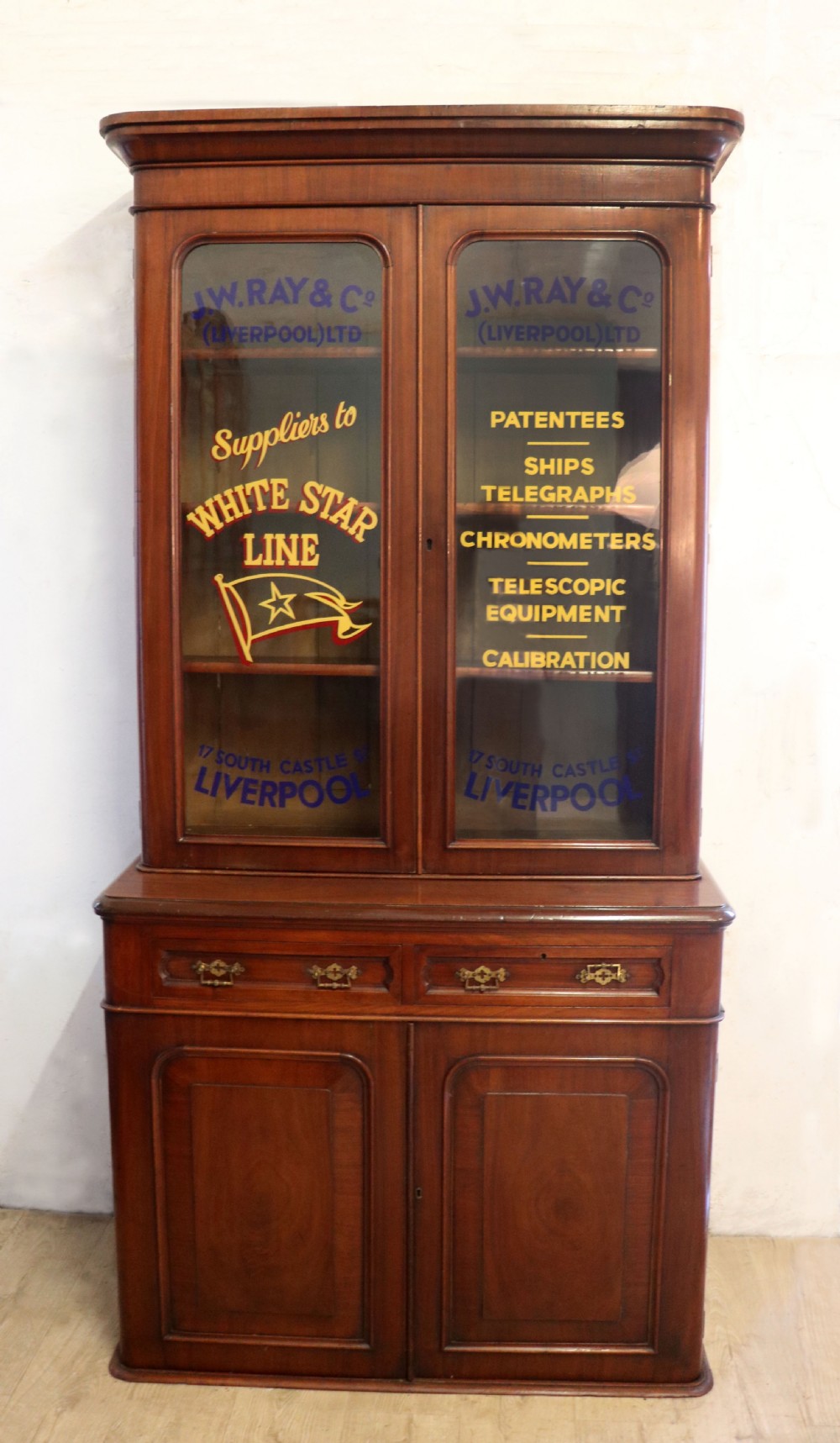A late Victorian mahogany two-piece bookcase cabinet featuring upper glazed doors with gilded advertising lettering above two frieze drawers and a cupboard base.