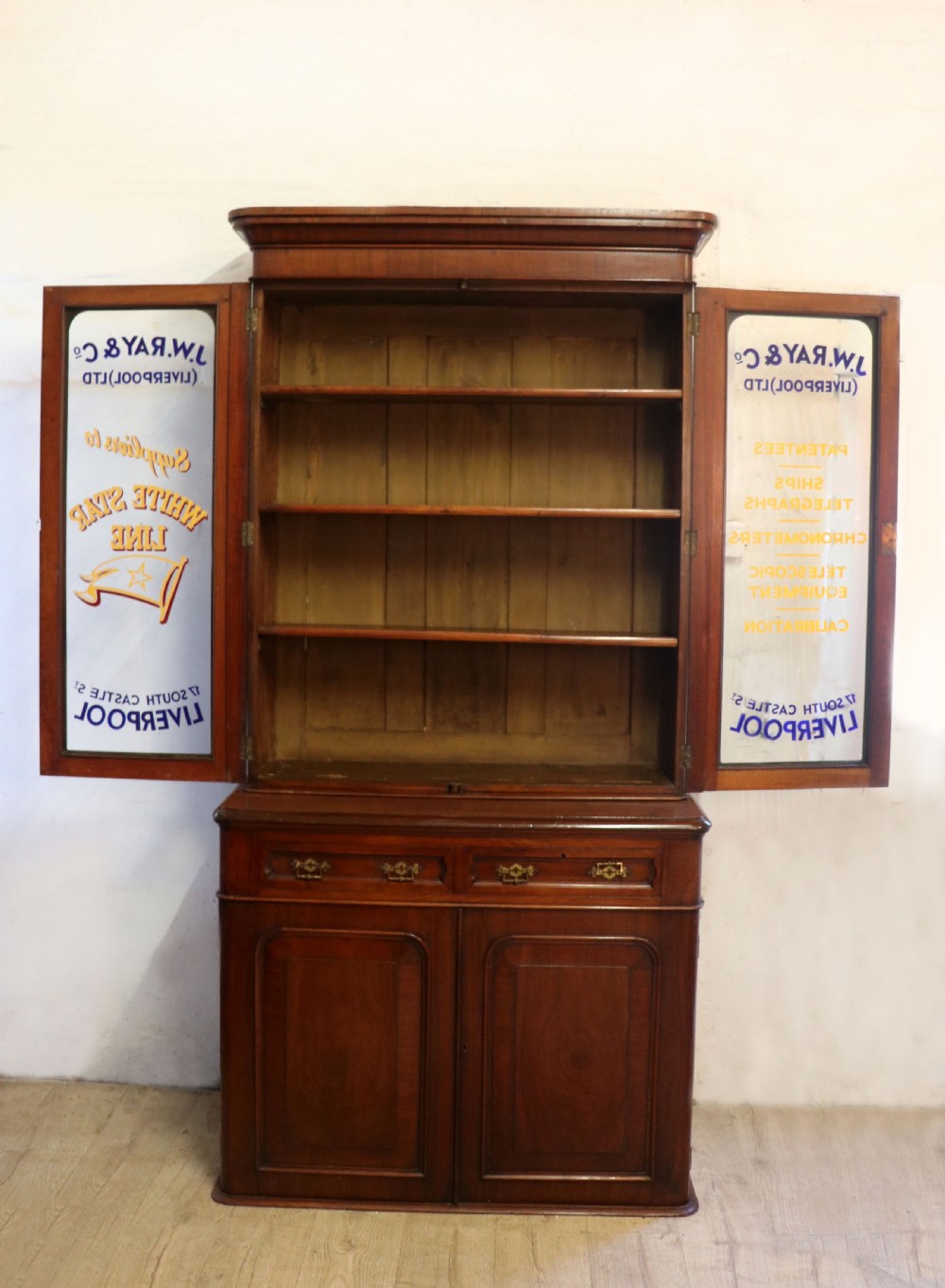 A late Victorian mahogany two-piece bookcase cabinet featuring upper glazed doors with gilded advertising lettering above two frieze drawers and a cupboard base. View II