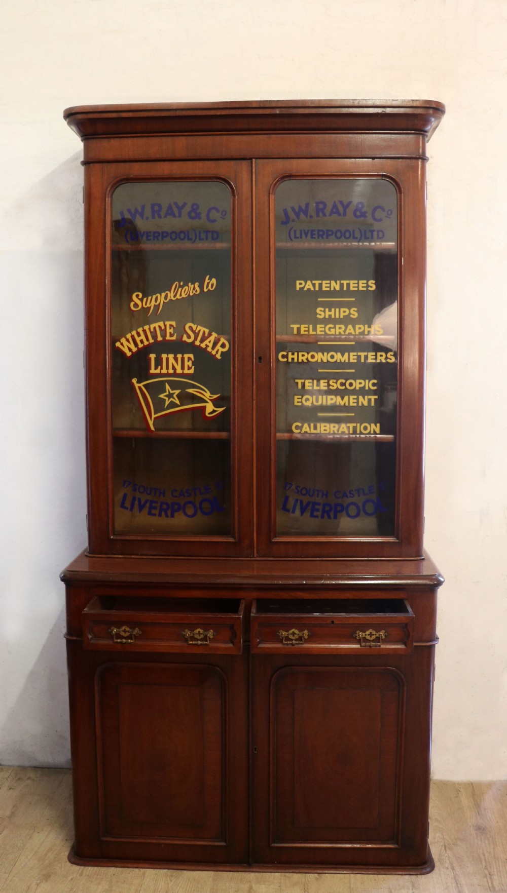 A late Victorian mahogany two-piece bookcase cabinet featuring upper glazed doors with gilded advertising lettering above two frieze drawers and a cupboard base. View III