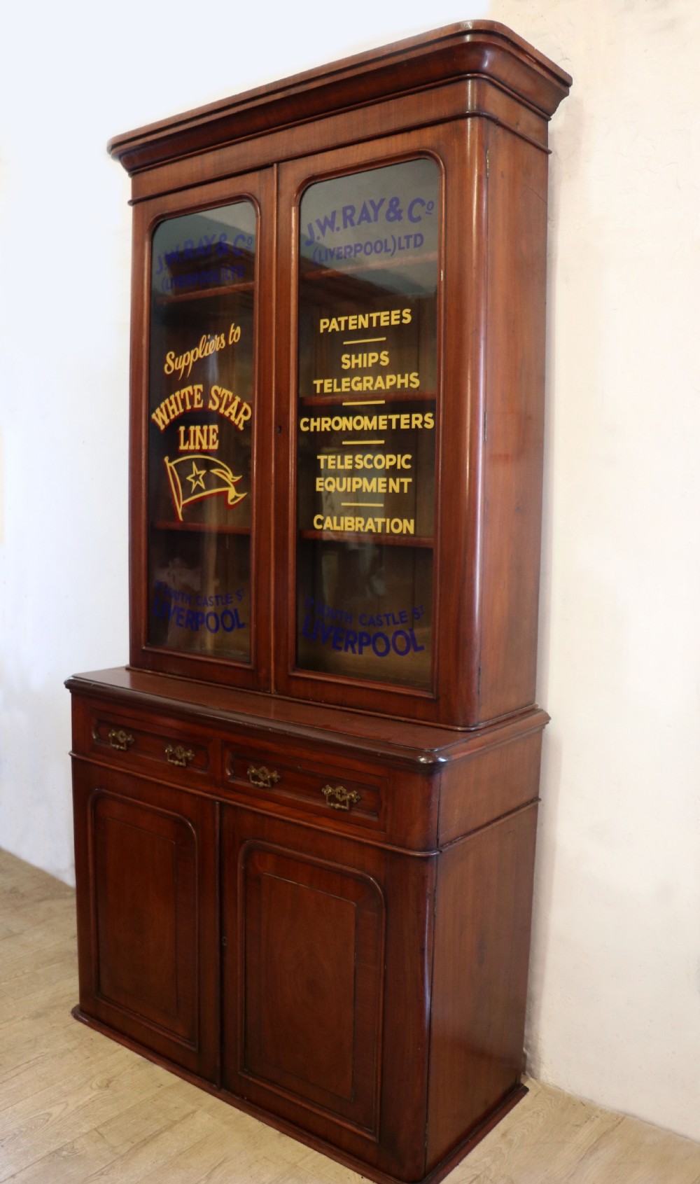 A late Victorian mahogany two-piece bookcase cabinet featuring upper glazed doors with gilded advertising lettering above two frieze drawers and a cupboard base. View VI