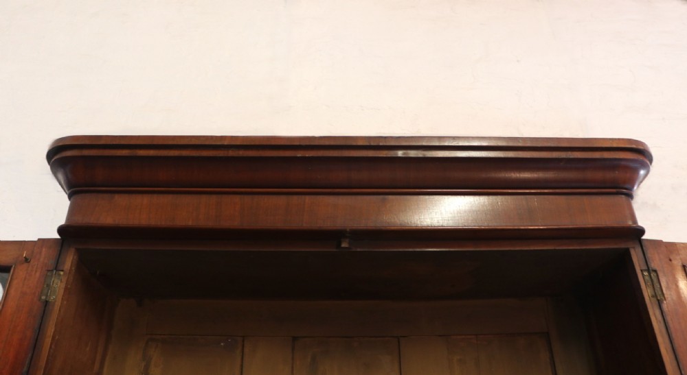 A late Victorian mahogany two-piece bookcase cabinet featuring upper glazed doors with gilded advertising lettering above two frieze drawers and a cupboard base. View VII