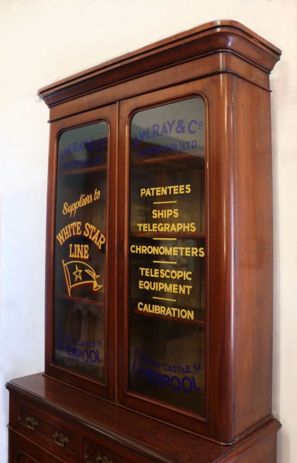 A late Victorian mahogany two-piece bookcase cabinet featuring upper glazed doors with gilded advertising lettering above two frieze drawers and a cupboard base. View VIII