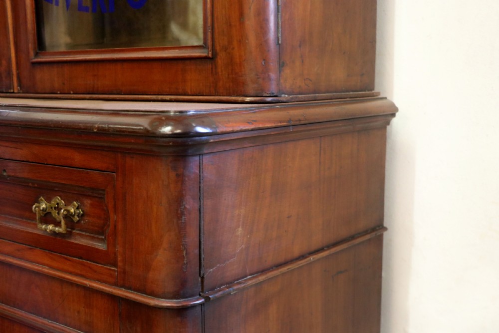 A late Victorian mahogany two-piece bookcase cabinet featuring upper glazed doors with gilded advertising lettering above two frieze drawers and a cupboard base. View XIII