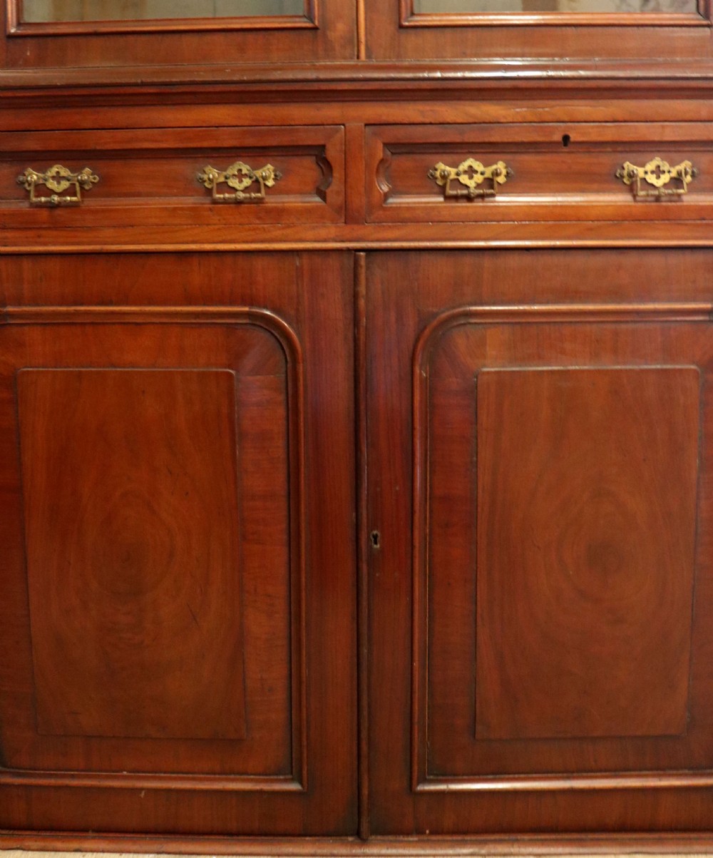 A late Victorian mahogany two-piece bookcase cabinet featuring upper glazed doors with gilded advertising lettering above two frieze drawers and a cupboard base. View XX