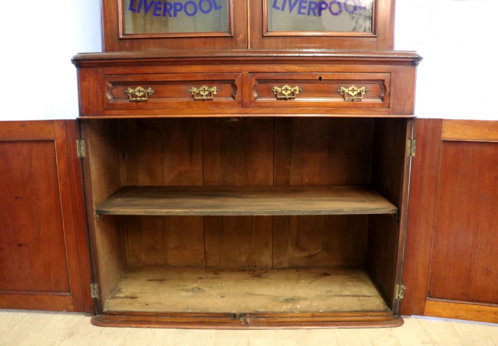 A late Victorian mahogany two-piece bookcase cabinet featuring upper glazed doors with gilded advertising lettering above two frieze drawers and a cupboard base. View XXI